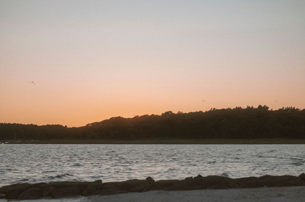 A stunning panoramic sequence of lakeside sunset views with rocky shores and silhouetted trees against an orange sky.