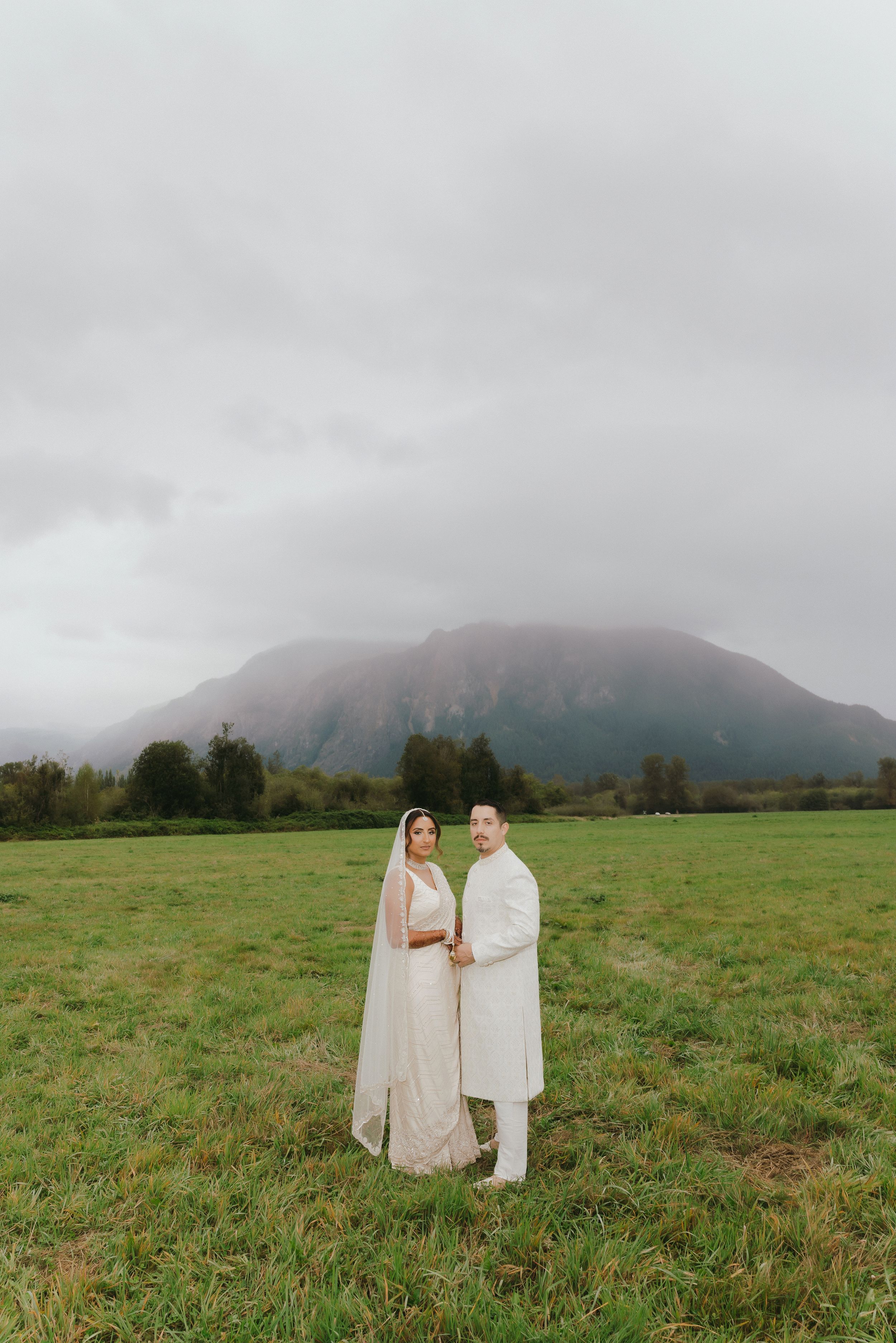 Two figures in white robes stand in a misty green field with mountains shrouded in clouds in the background.