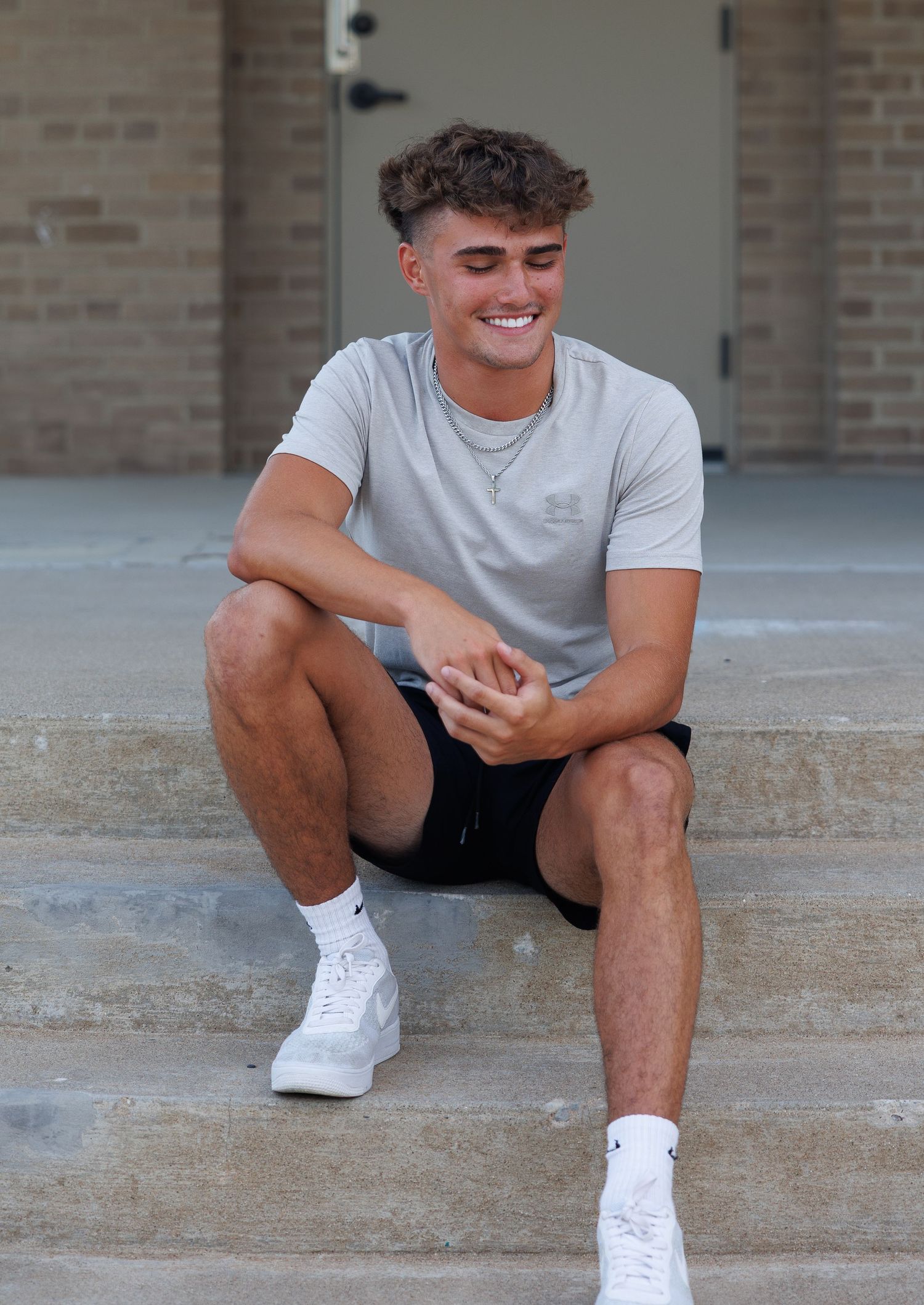 A person wearing a light grey t-shirt and black shorts sits on concrete steps while looking at their phone.