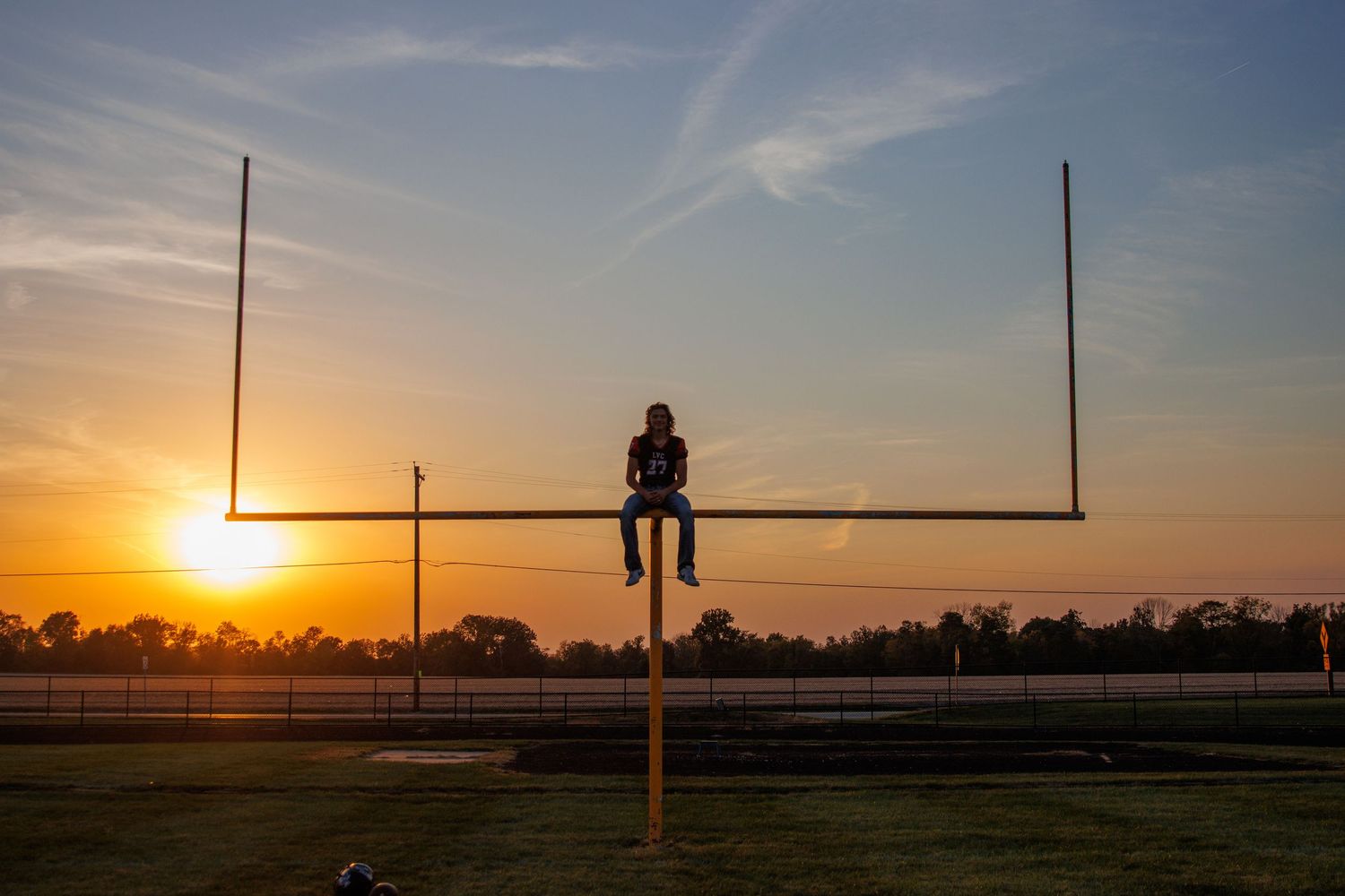 Silhouette of person sitting on football goalpost at sunset. Senior boy sitting on football goalpost.