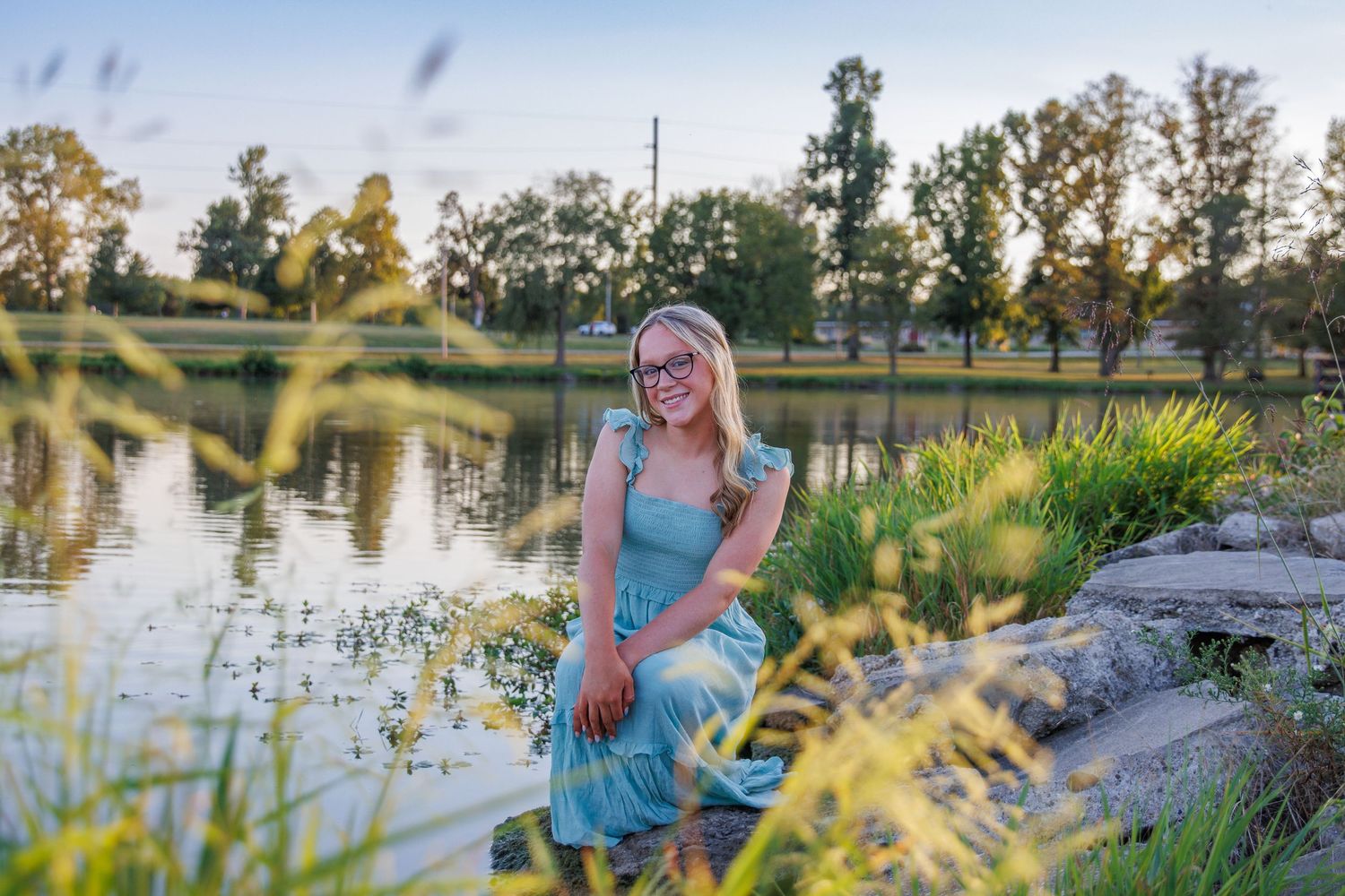 Dreamy summer portrait by a pond with tall grass and trees at golden hour.