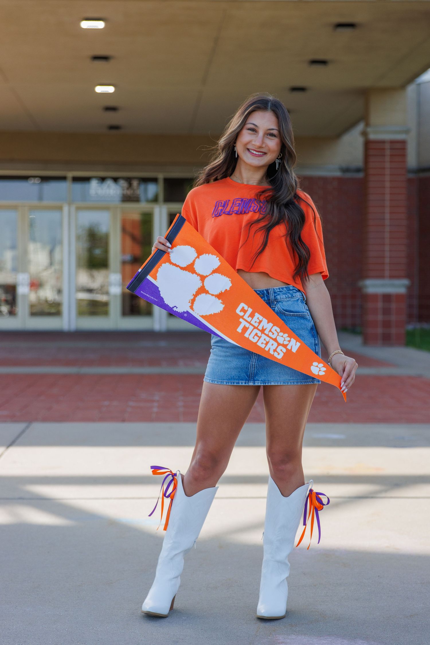 Clemson University sports fan posing with team pennant in white boots and orange shirt. Senior girl holding Clemson University pennant.