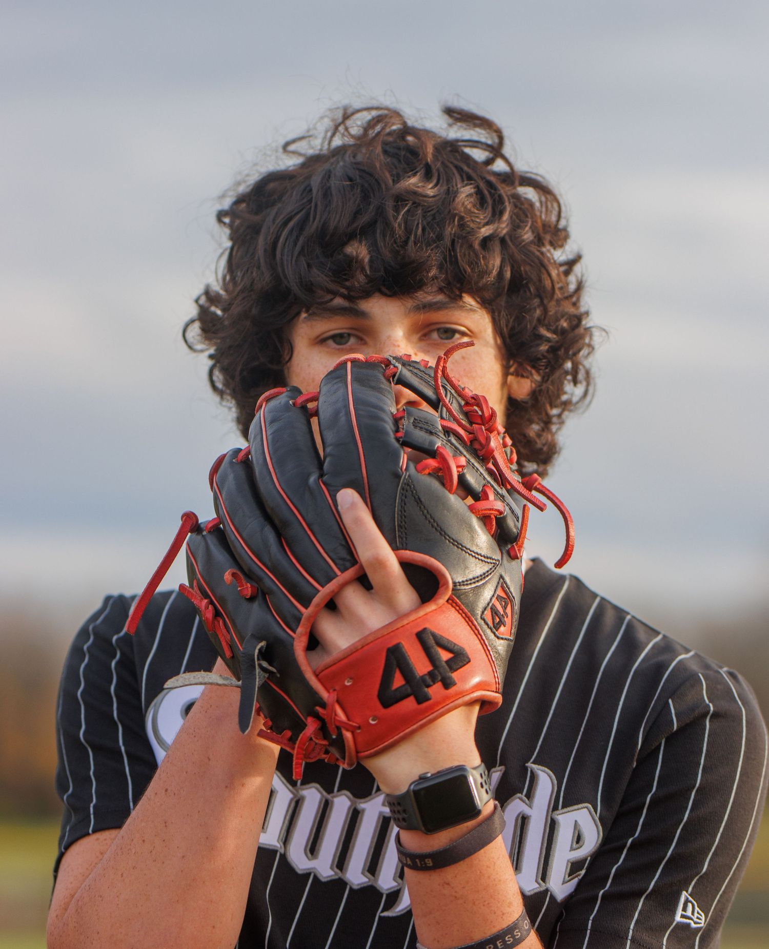 Baseball player wearing pinstripe uniform holding up glove to face. Senior boy posed for baseball photoshoot.