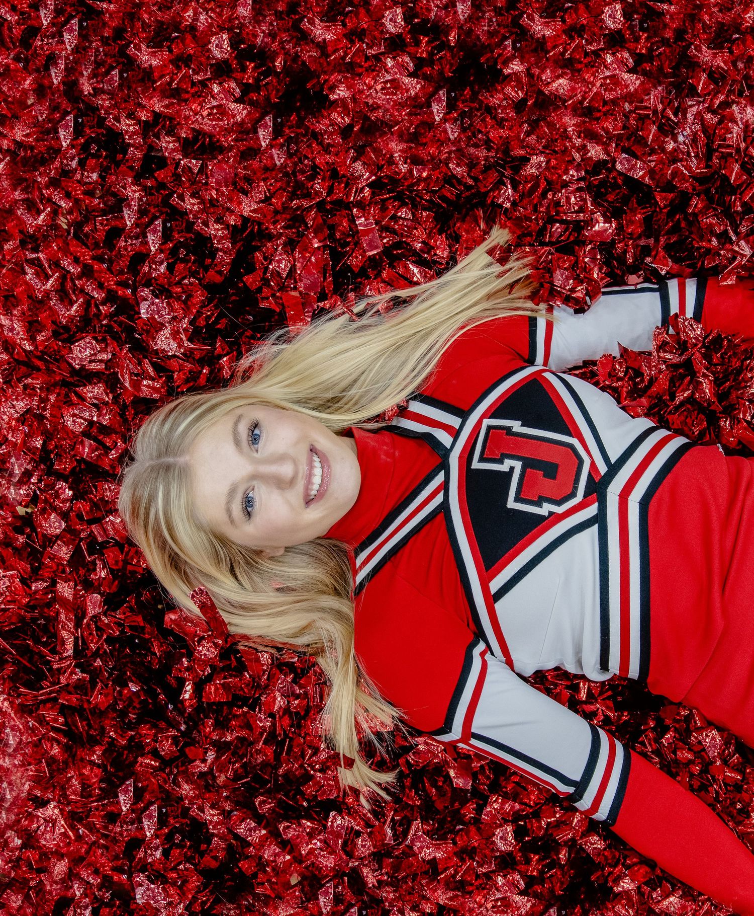 A cheerleader in red and white uniform poses on red pom poms in a creative photo composition.