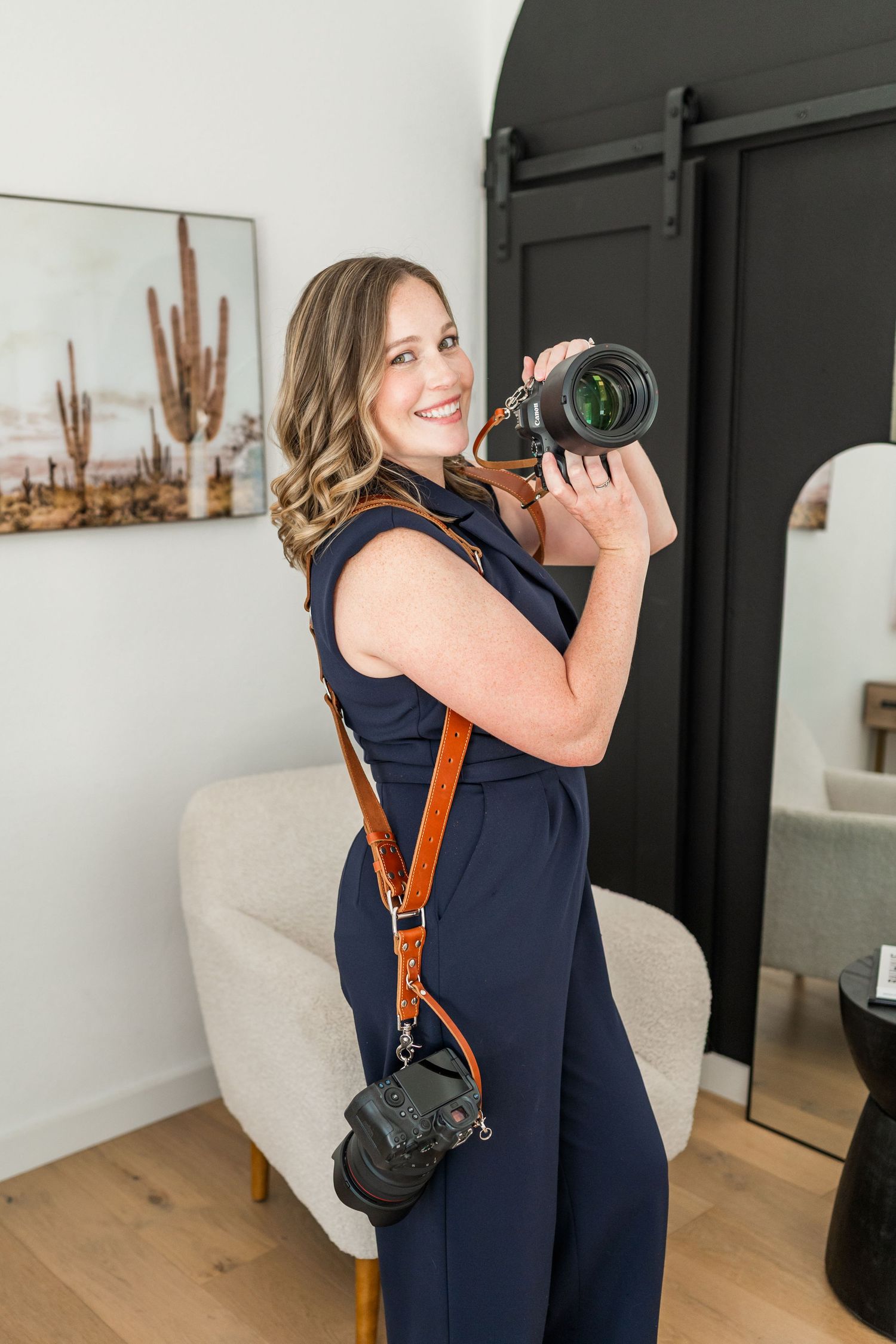 Professional photographer in blue floral dress holding camera in pink room.