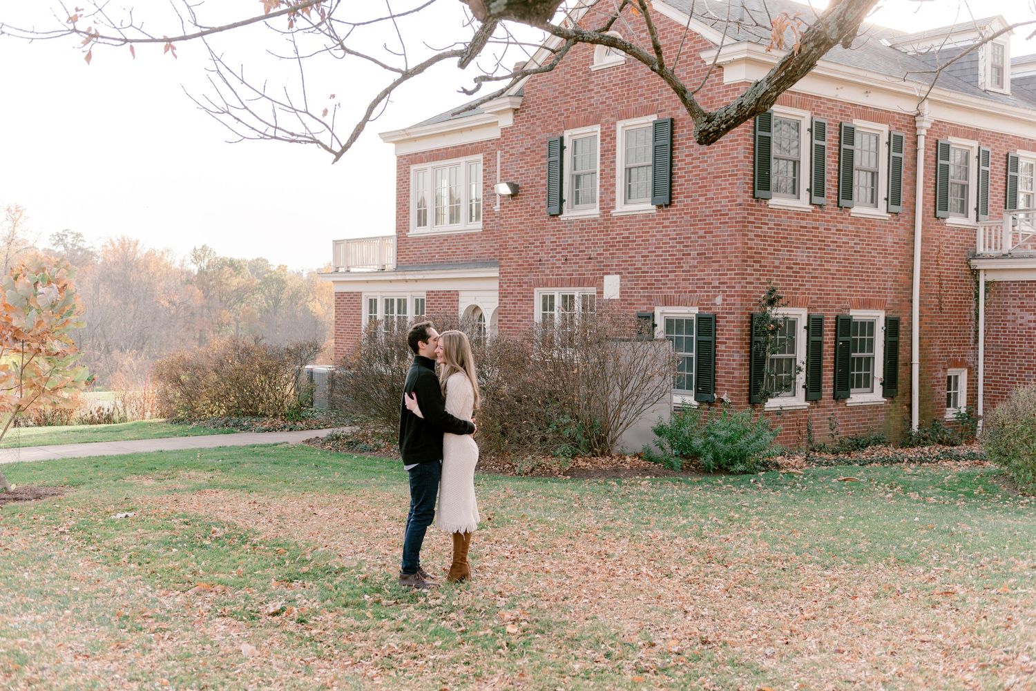 A couple embraces in front of a brick building on an autumn day.