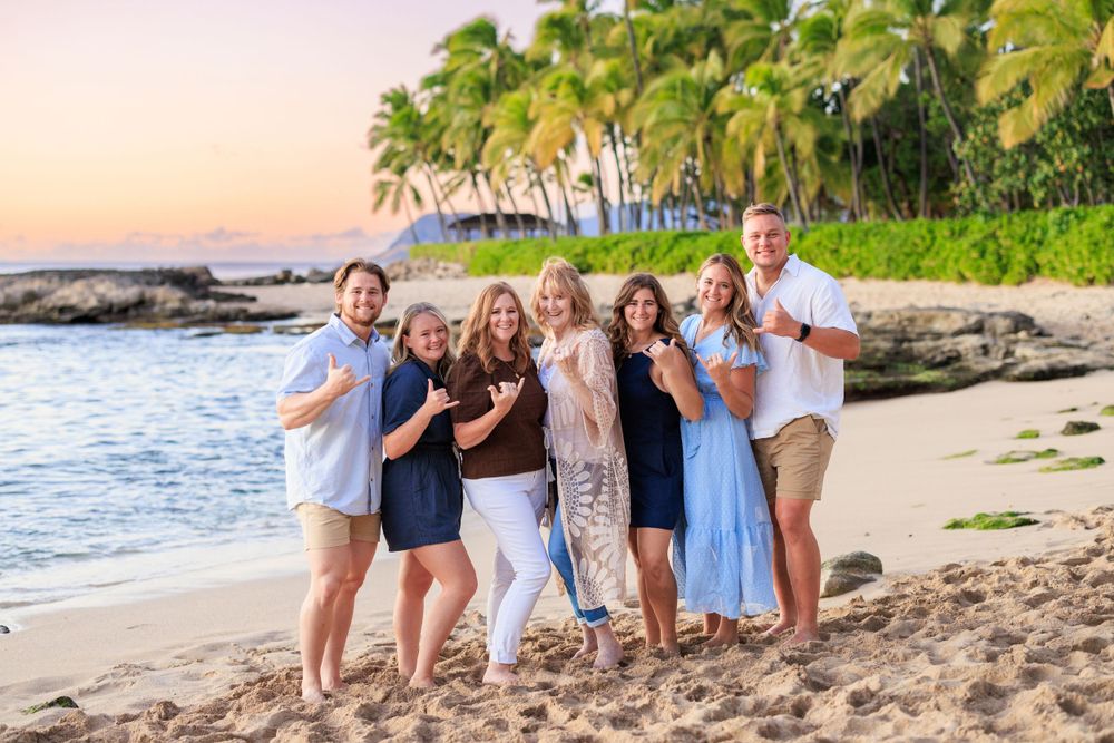 Family group posing on a tropical beach at sunset with palm trees and ocean in the background.