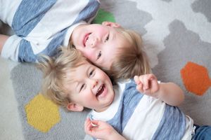 Two happy toddlers lying on a colorful patterned rug, laughing and smiling together.