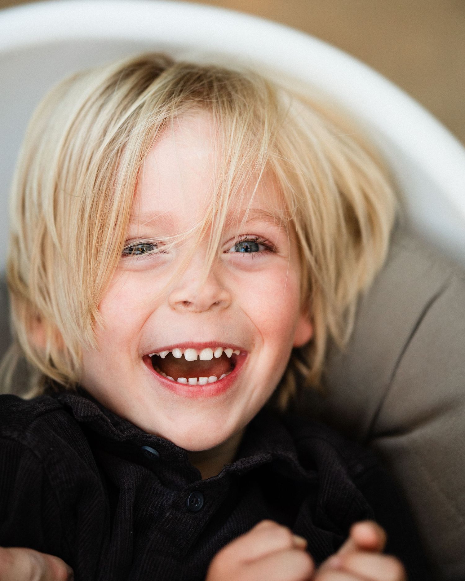 A happy blonde child laughs with a big smile, showing missing teeth, wearing a black jacket.