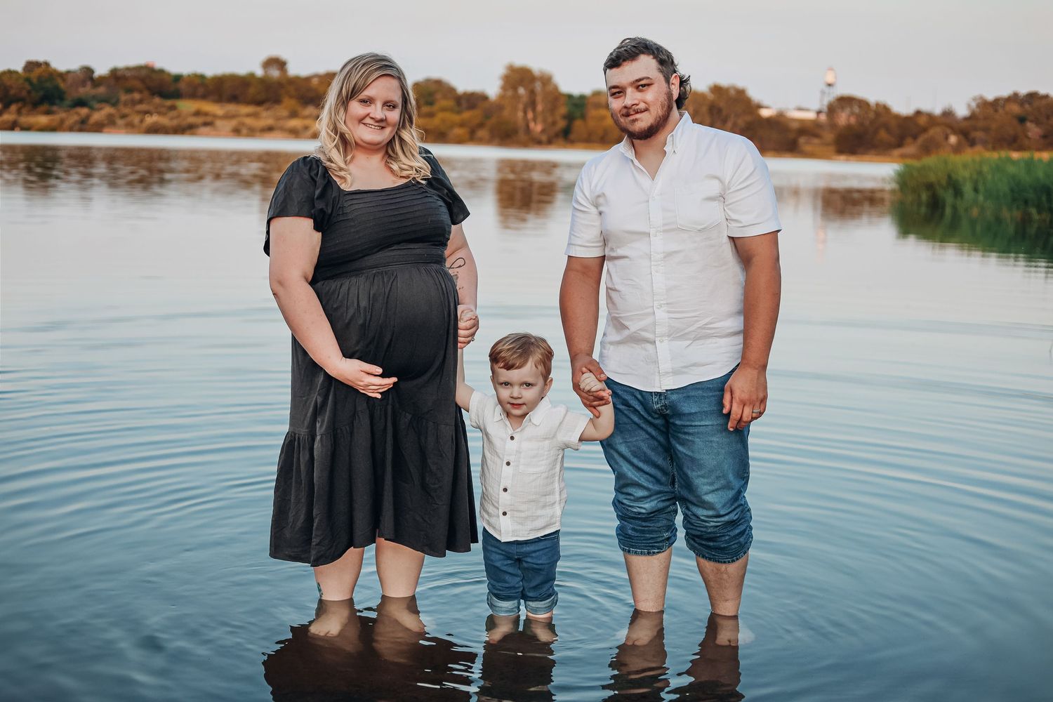 Family standing in shallow water at sunset by lake. Maternity photography