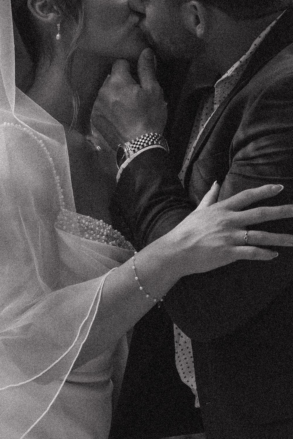 Black and white wedding photo of bride and groom sharing a kiss, bride wearing veil and bracelet, groom in suit.
