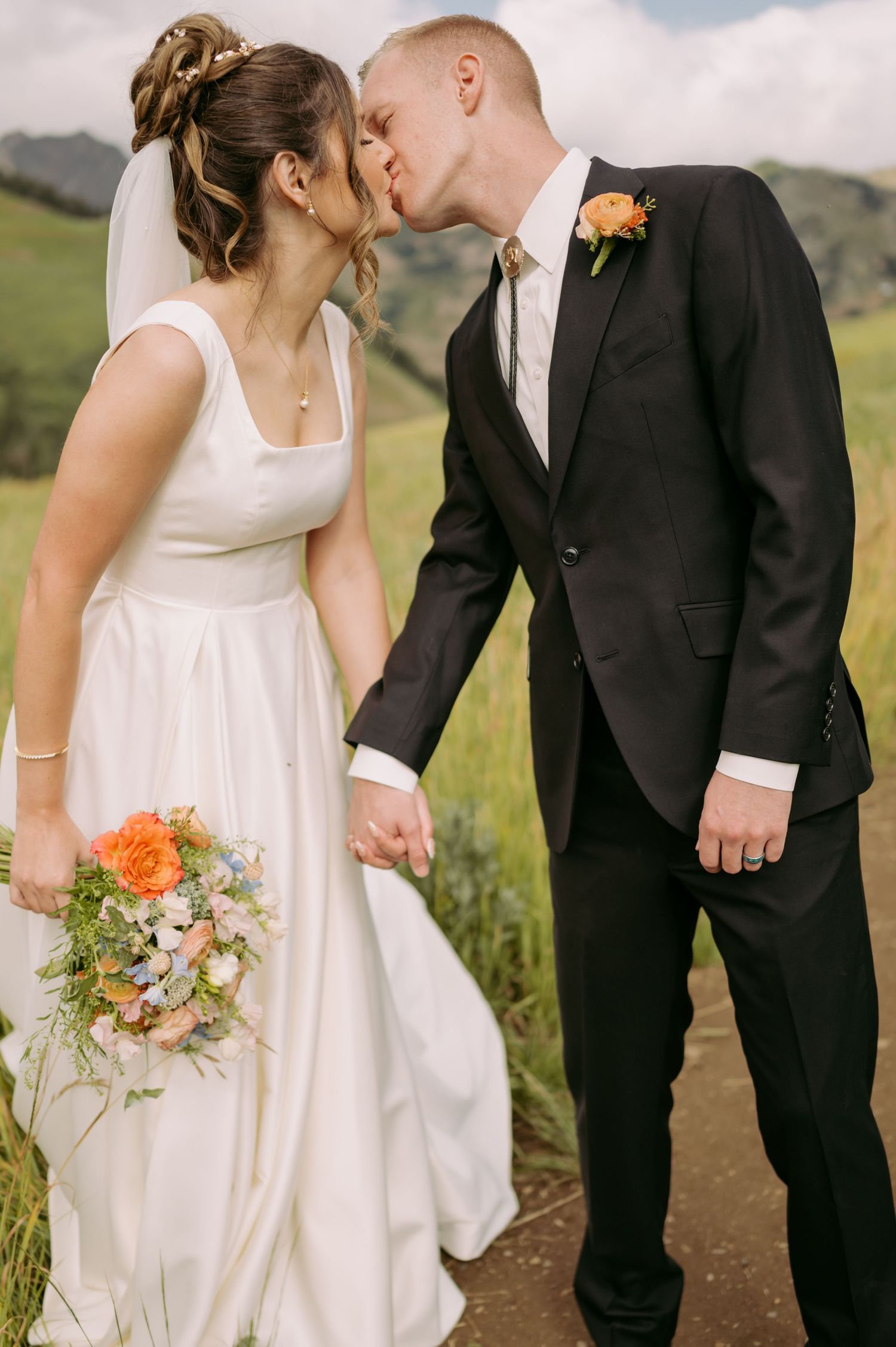 Intimate wedding portrait of couple sharing tender moment on mountain path.