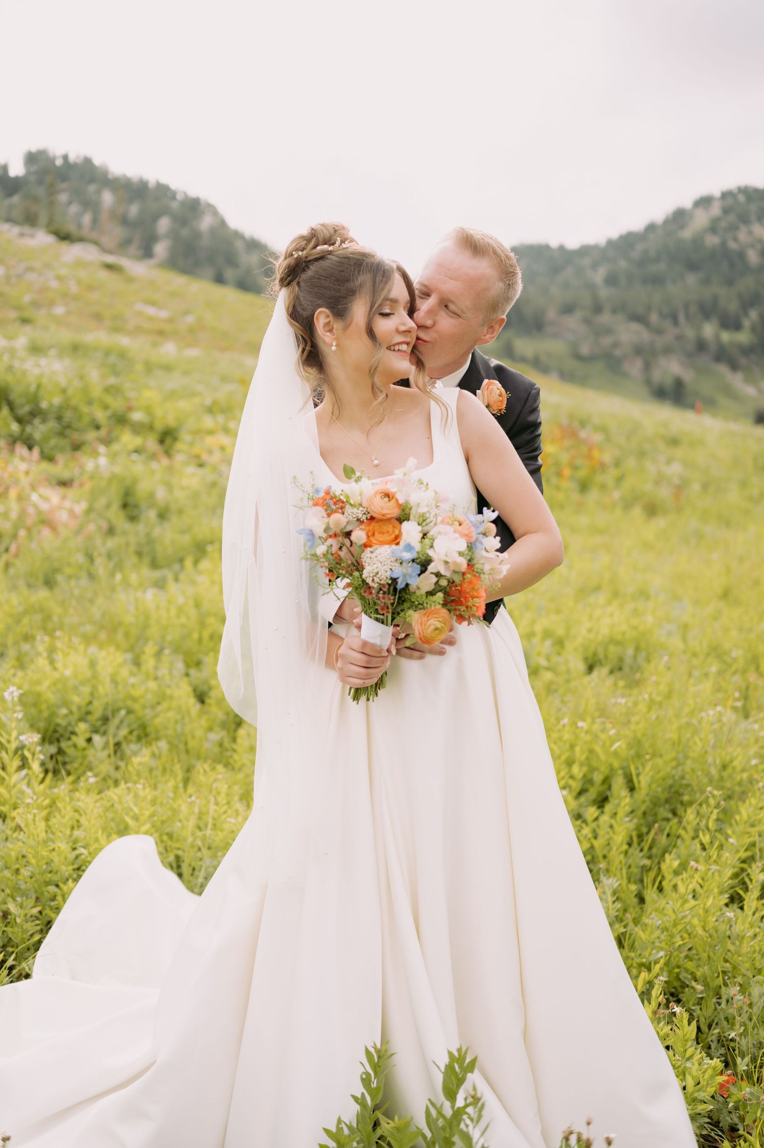 A couple shares a romantic moment in their wedding attire amid a scenic mountain meadow.