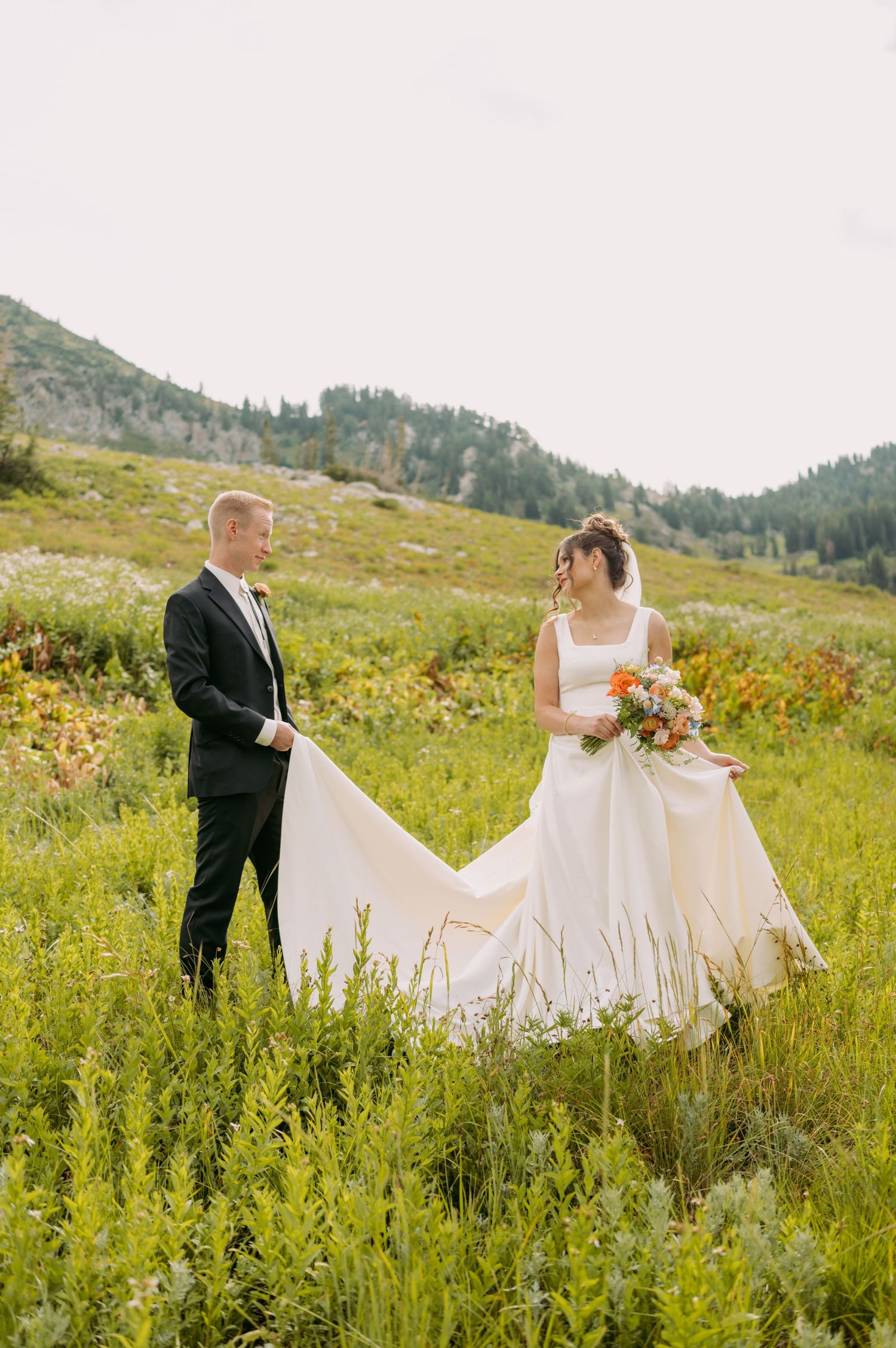 Wedding couple poses in a mountain meadow with flowing white dress and wildflowers.