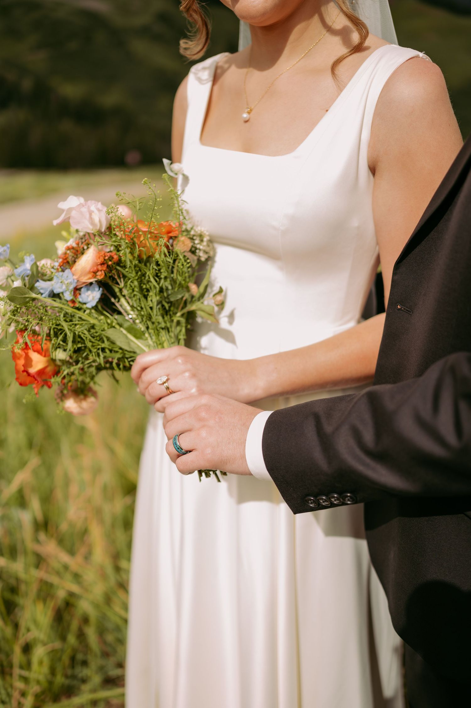 Wedding couple holds a delicate bouquet of orange and white flowers against natural scenery.
