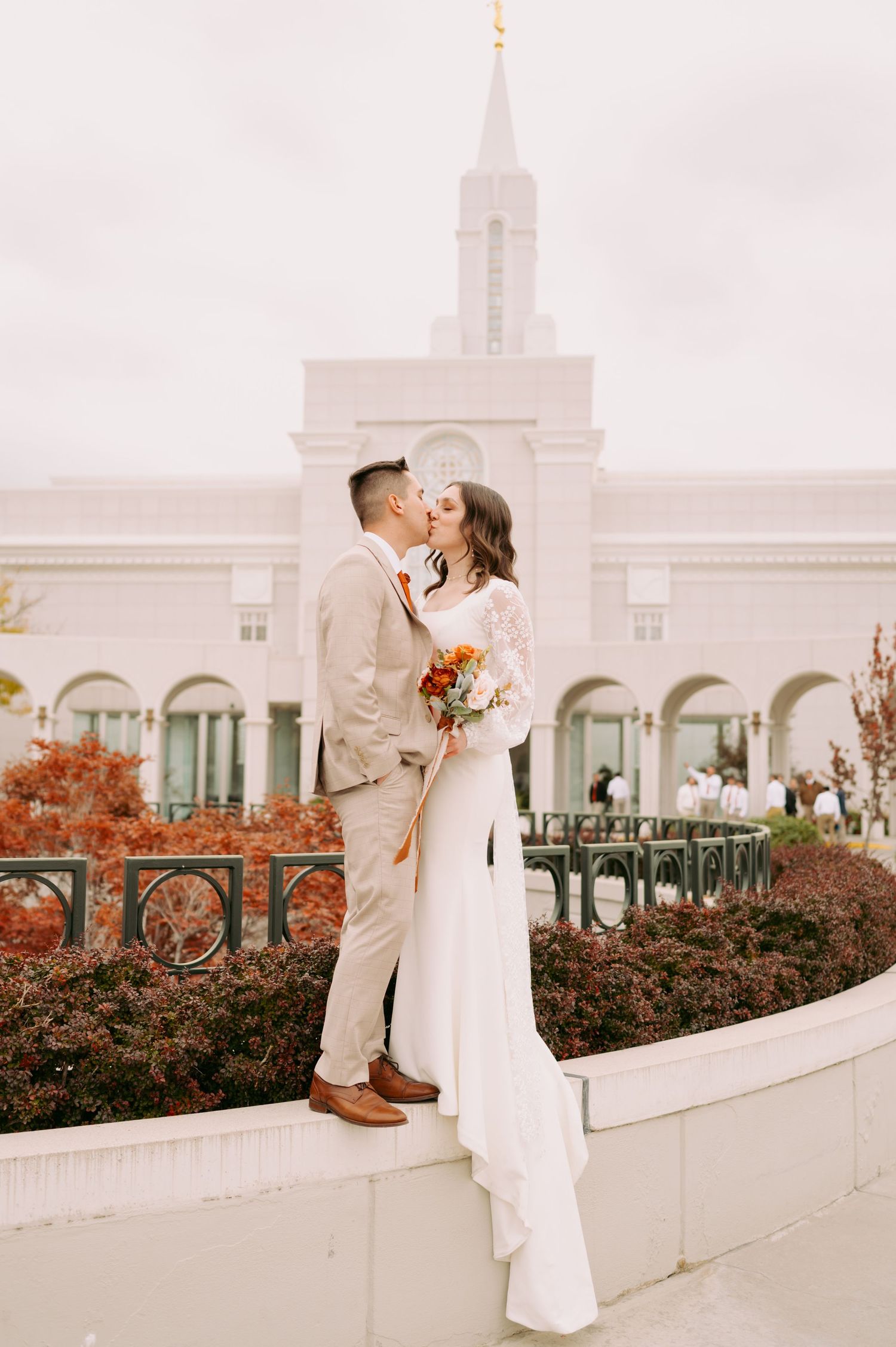Romantic wedding portrait in front of a white temple building with fall foliage.