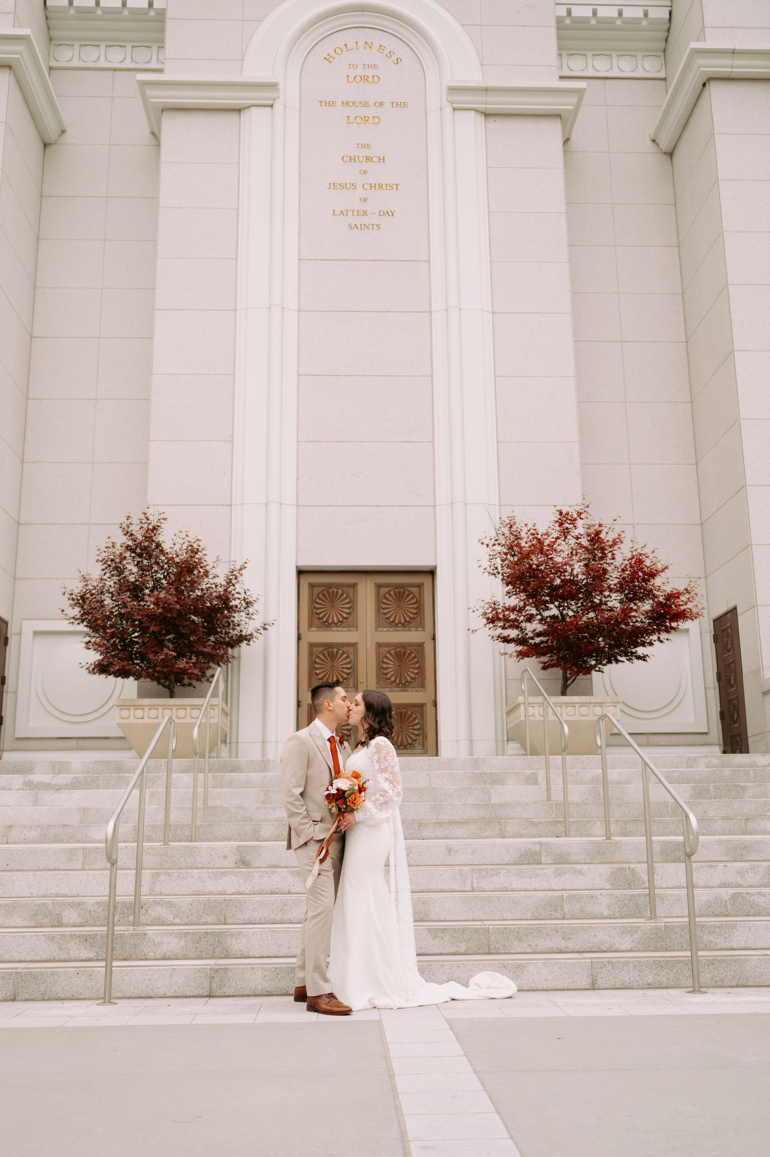A white temple facade with grand steps and two red maple trees framing the entrance doors.