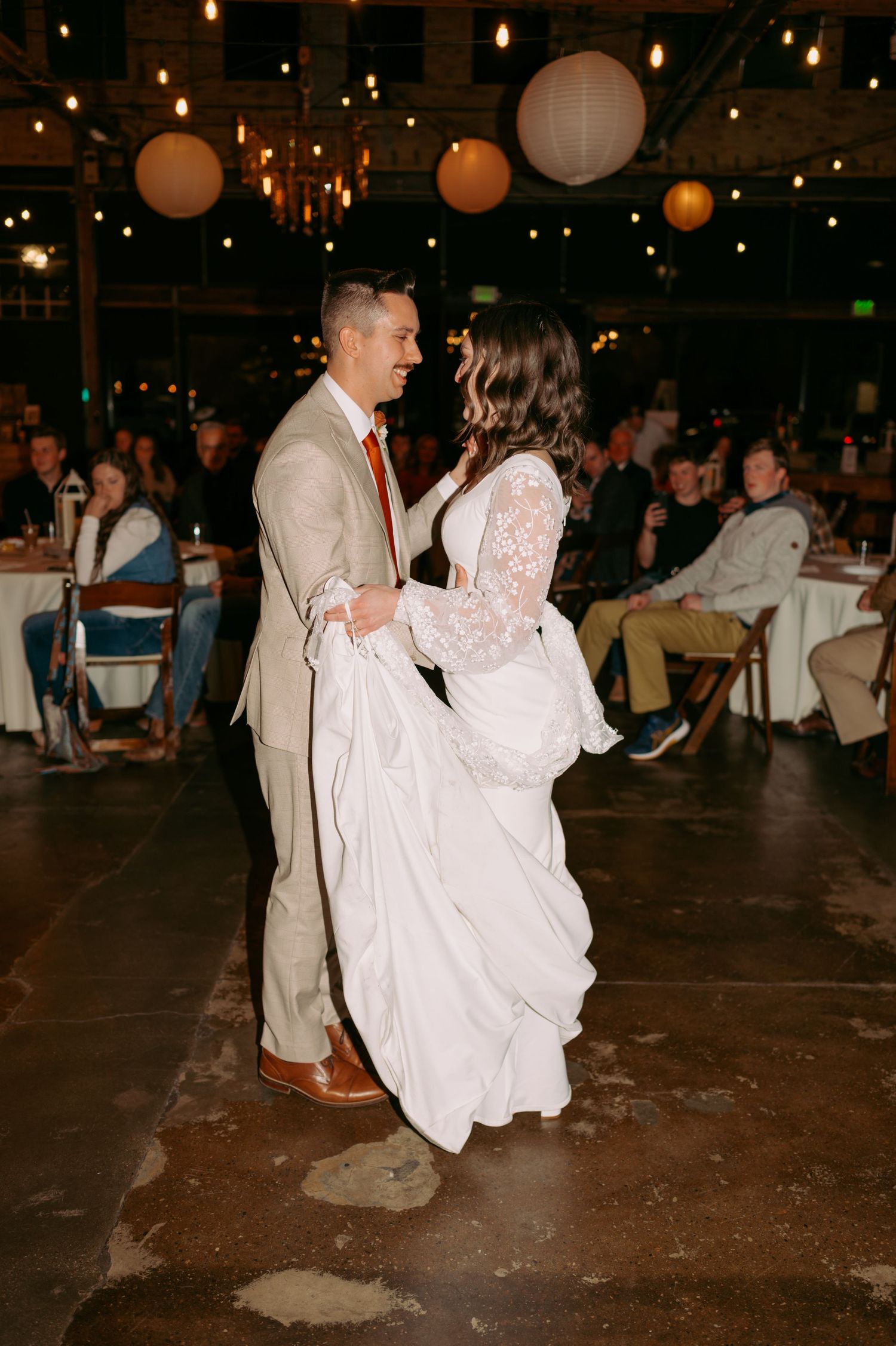 A couple dancing together on a rustic floor under glowing paper lanterns at their wedding reception.