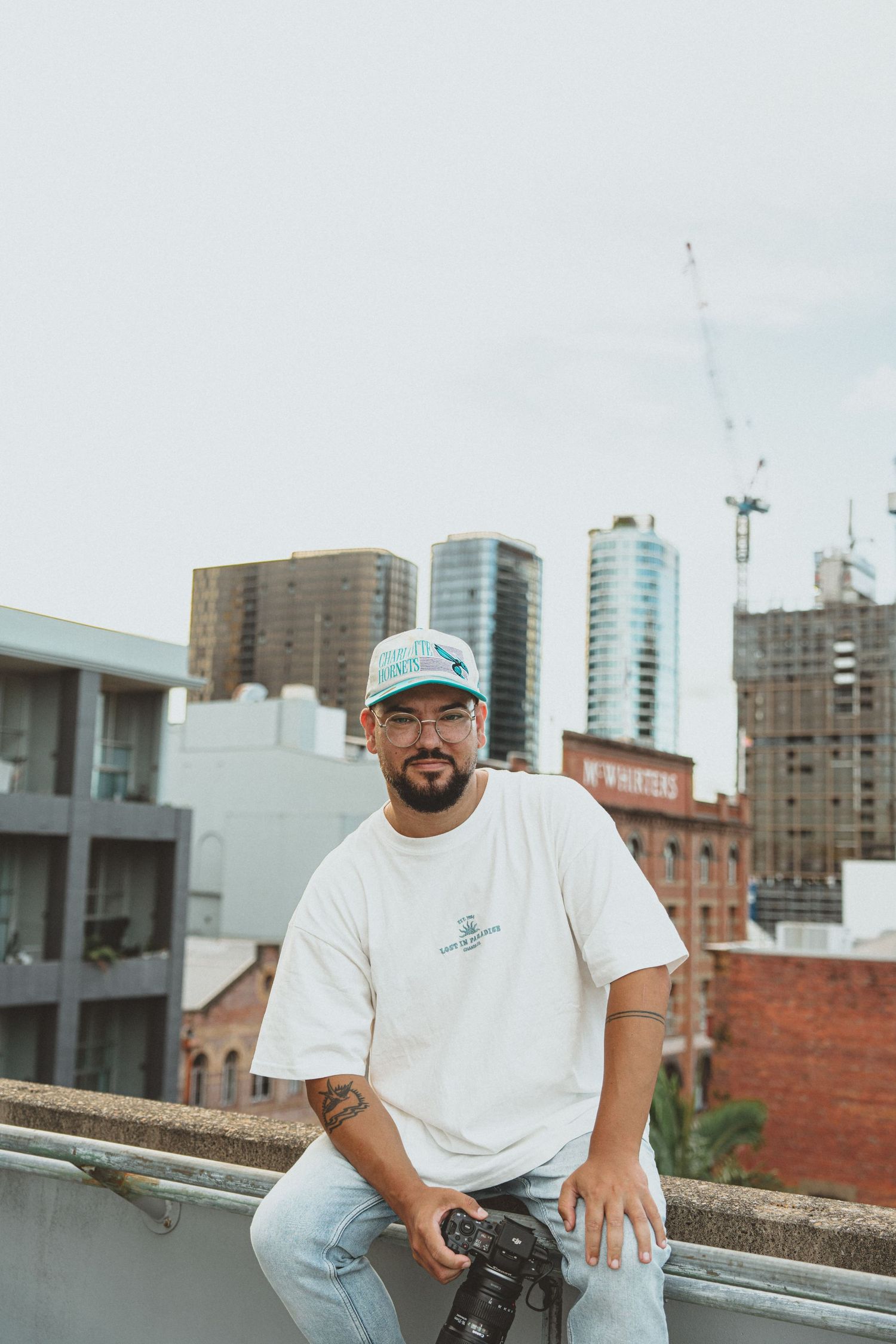 Casual portrait on urban rooftop with city skyline and construction cranes in background.