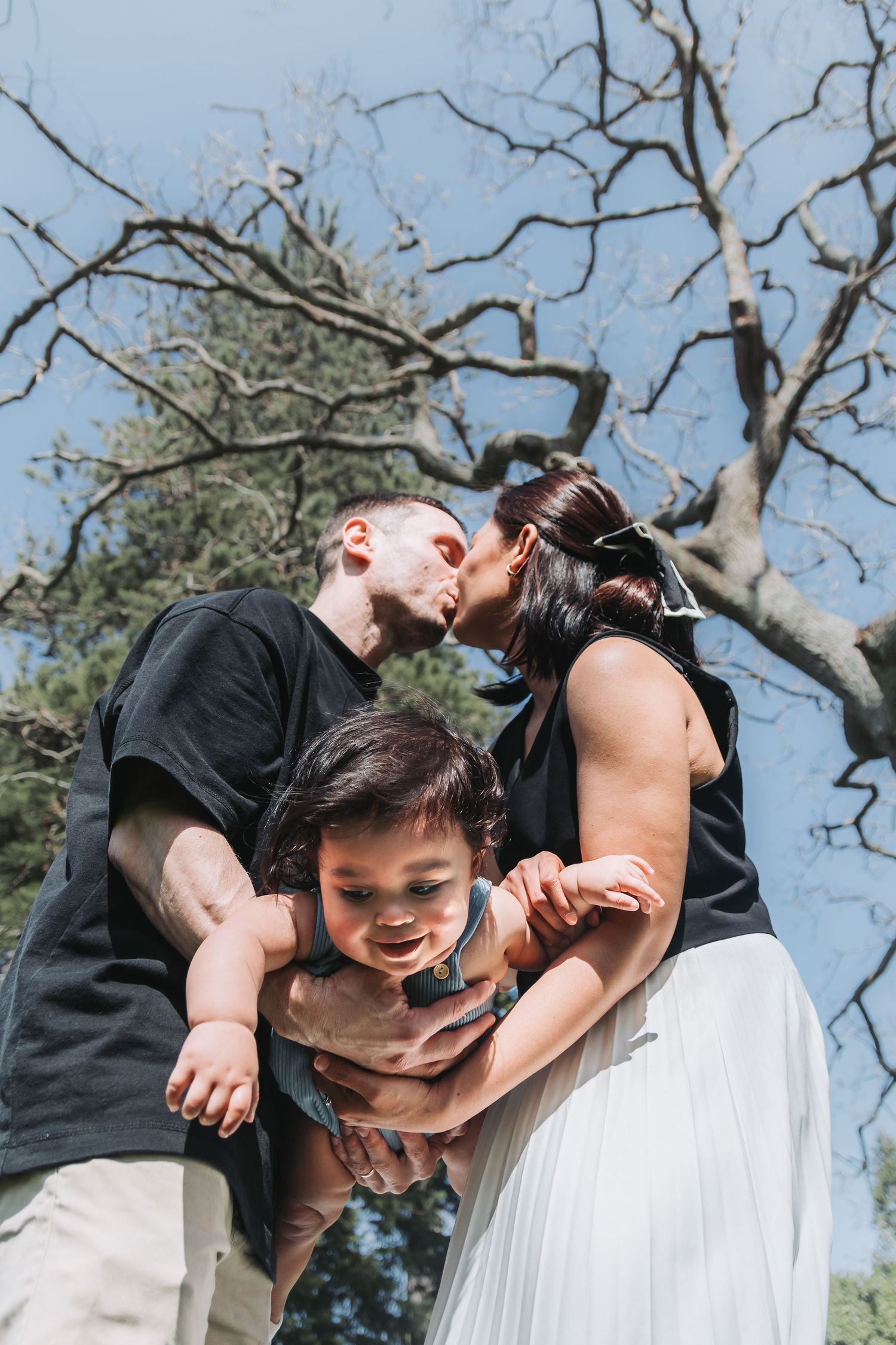 A joyful outdoor family moment captured against bare tree branches and blue sky.