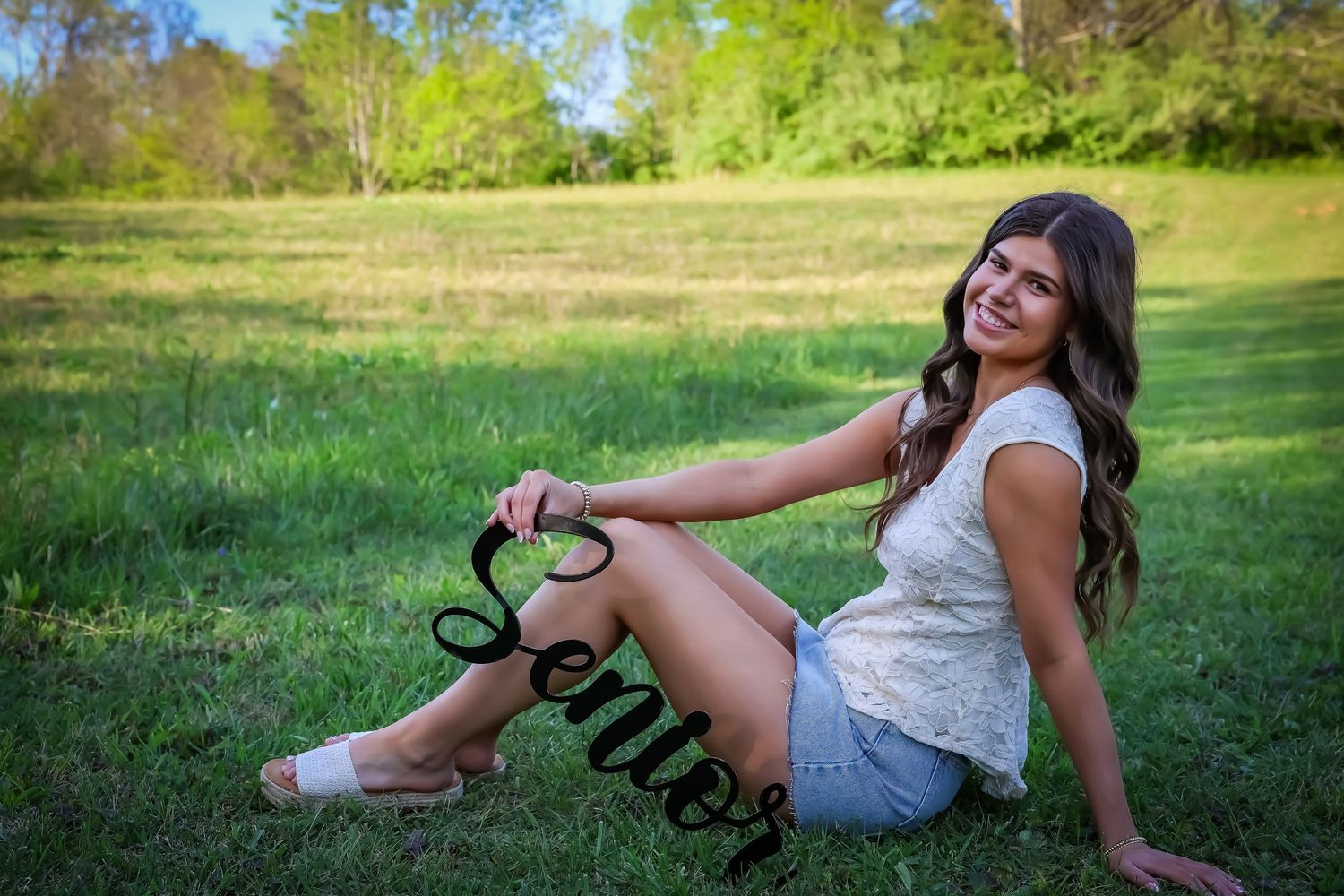 Woman in white dress poses casually on grass during an outdoor photo session.
