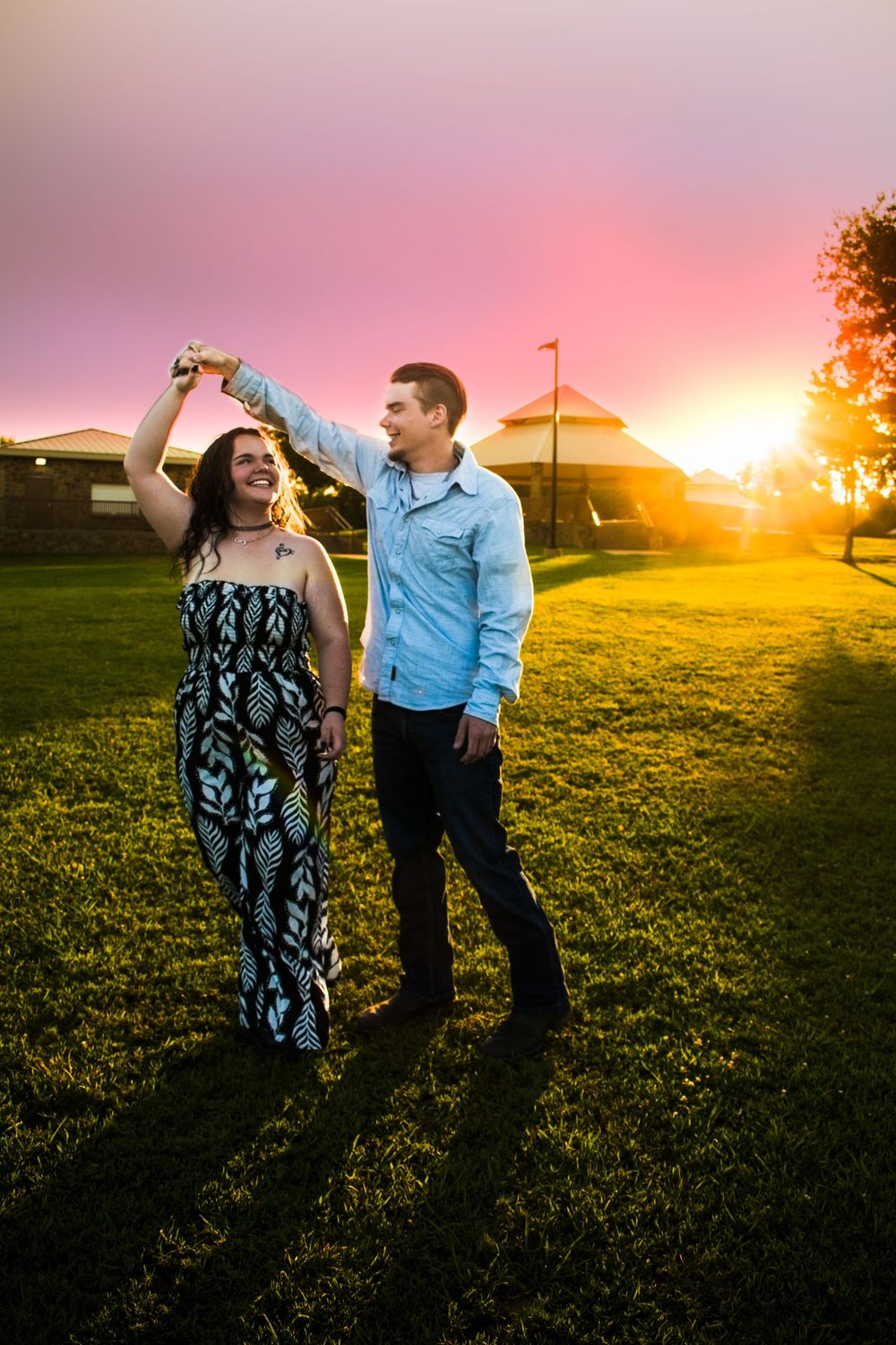 Couple shares a romantic moment in a grassy field at golden sunset with warm orange light illuminating the landscape.