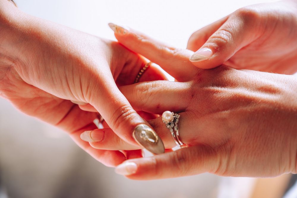 Close-up of two women's hands as one places a diamond engagement ring on the other's finger.