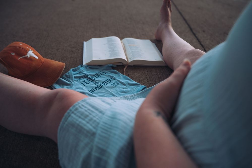 Person relaxing on floor with open book, blue shirt, and orange shoe beside bare feet.