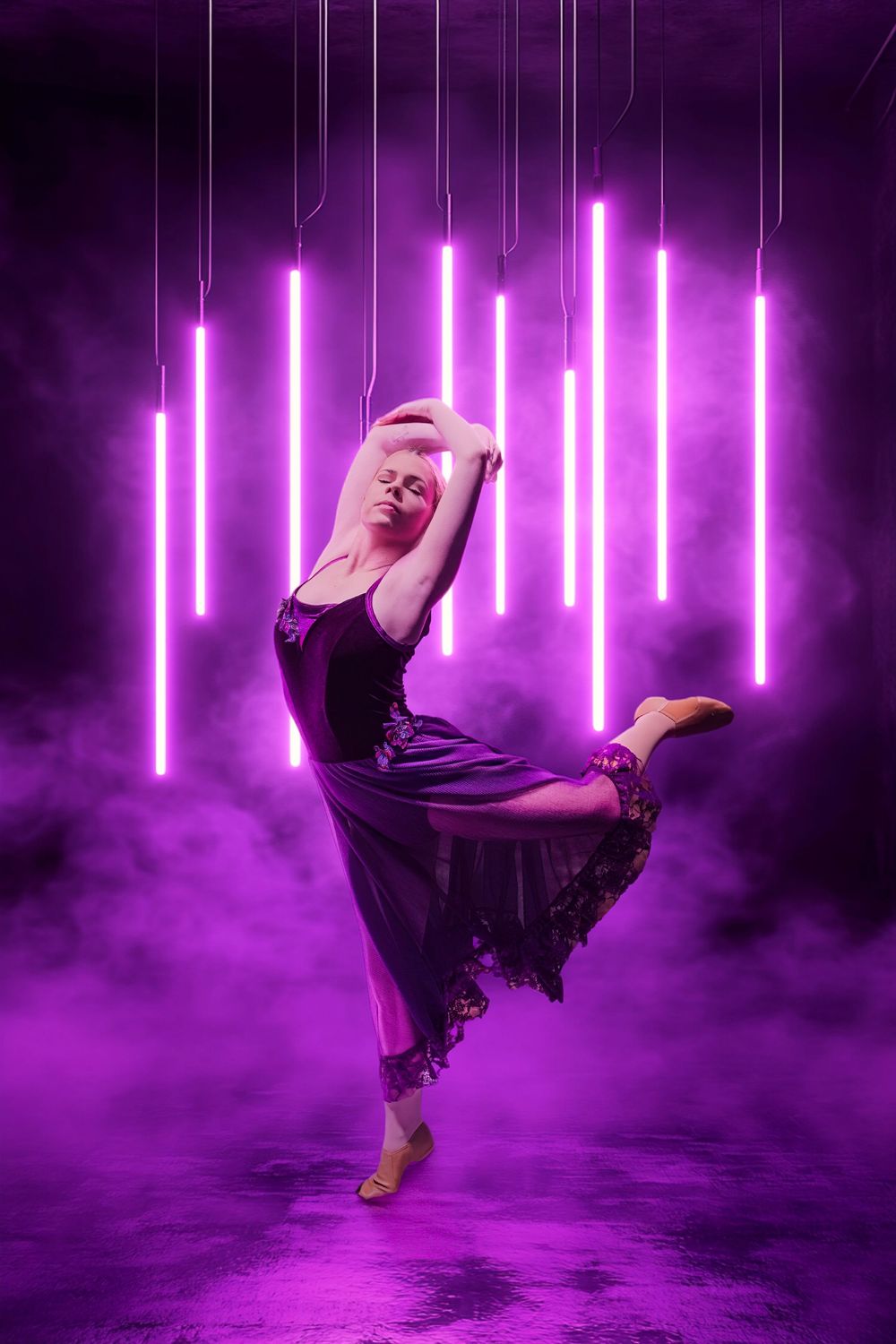 A graceful dancer poses elegantly in a purple-lit studio with glowing neon tubes and atmospheric smoke.