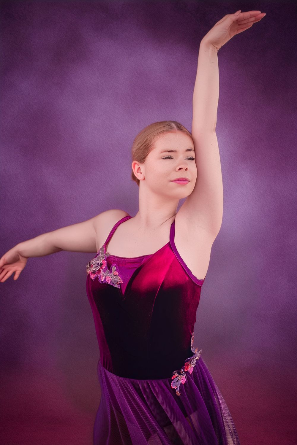 A young ballerina in a purple and red velvet costume gracefully poses with one arm raised against a purple background.