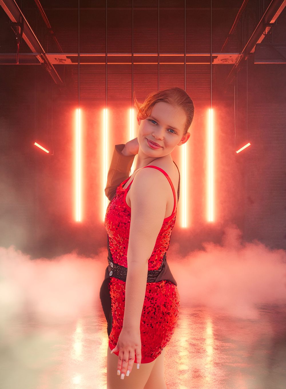 Young woman in red sequin dress poses confidently against glowing neon lights with dramatic red fog.