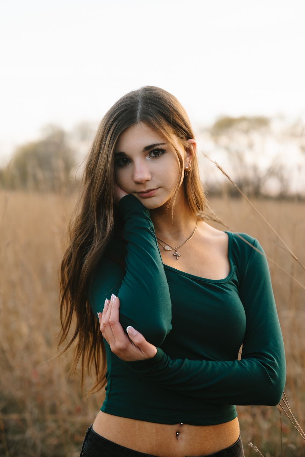 Portrait of a woman in a green crop top posing in a golden field at sunset.