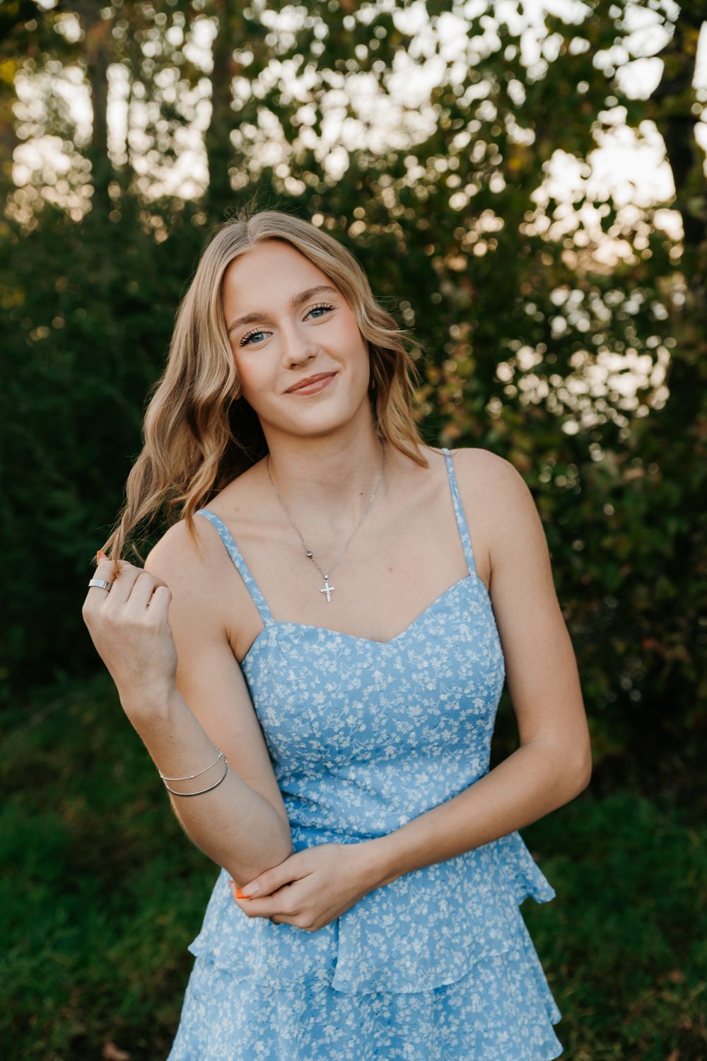Portrait of woman in blue floral sundress posing outdoors at sunset.