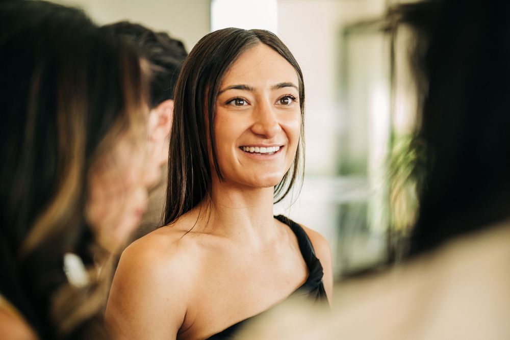 Young woman with long dark hair smiling warmly during a social gathering indoors.