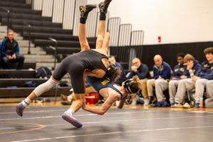 Two wrestlers competing during match on orange mat in gymnasium.