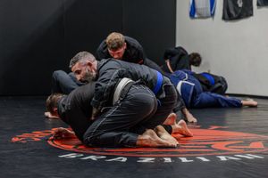 Martial artists practicing grappling techniques on black mats during training session.