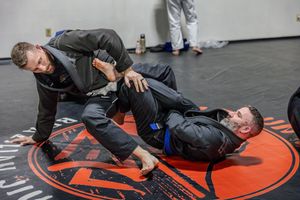 Jiu-jitsu practitioners sparring on orange and black mats during training.