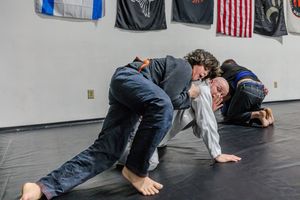 Students practicing grappling techniques on a martial arts gym floor with flags on the wall.