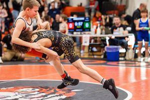 Two wrestlers compete in an intense match on an orange mat during a tournament.
