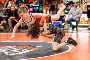 Dynamic wrestling match action shot showing two competitors grappling on an orange mat.