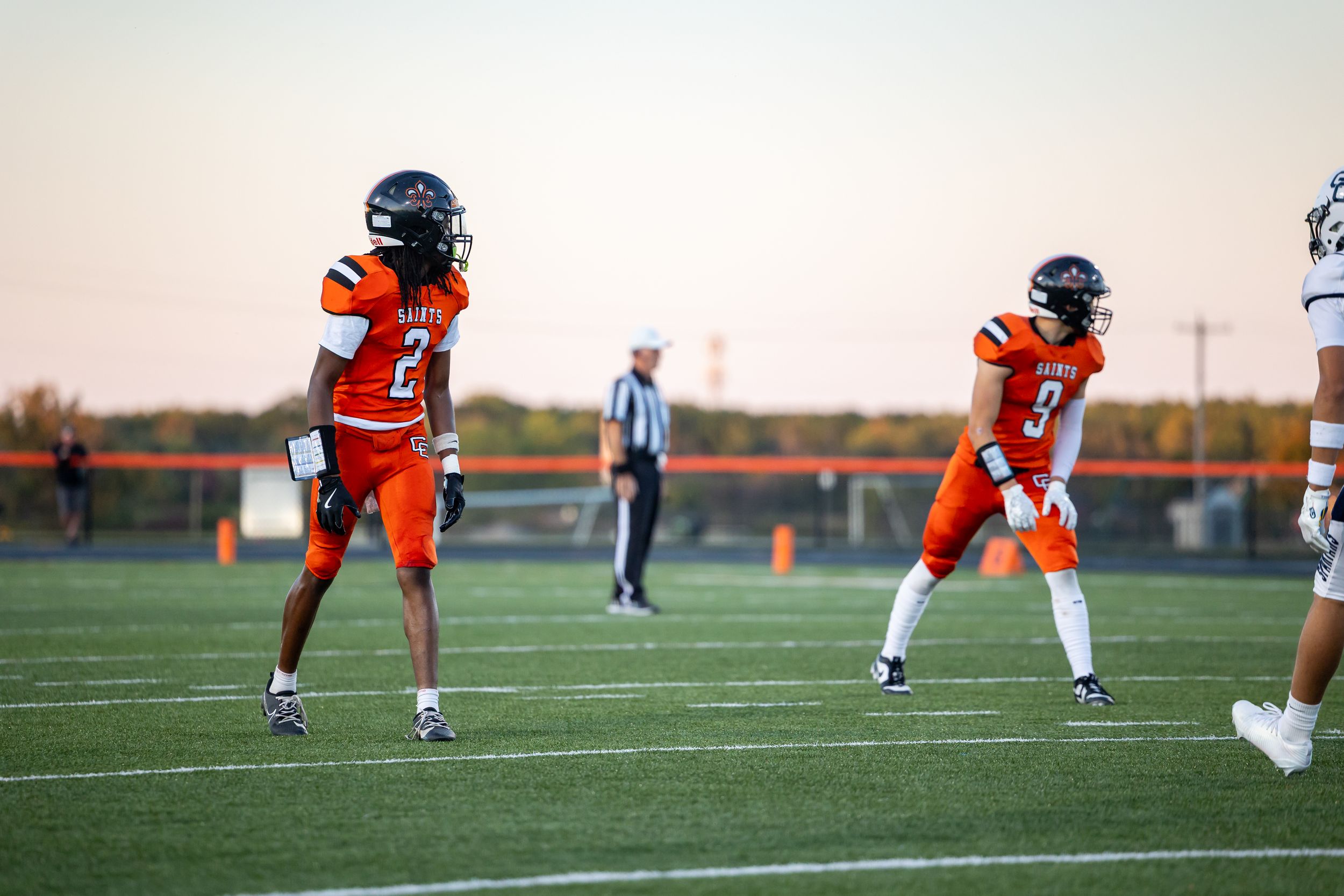 Football players in orange and white uniforms line up on field during game.