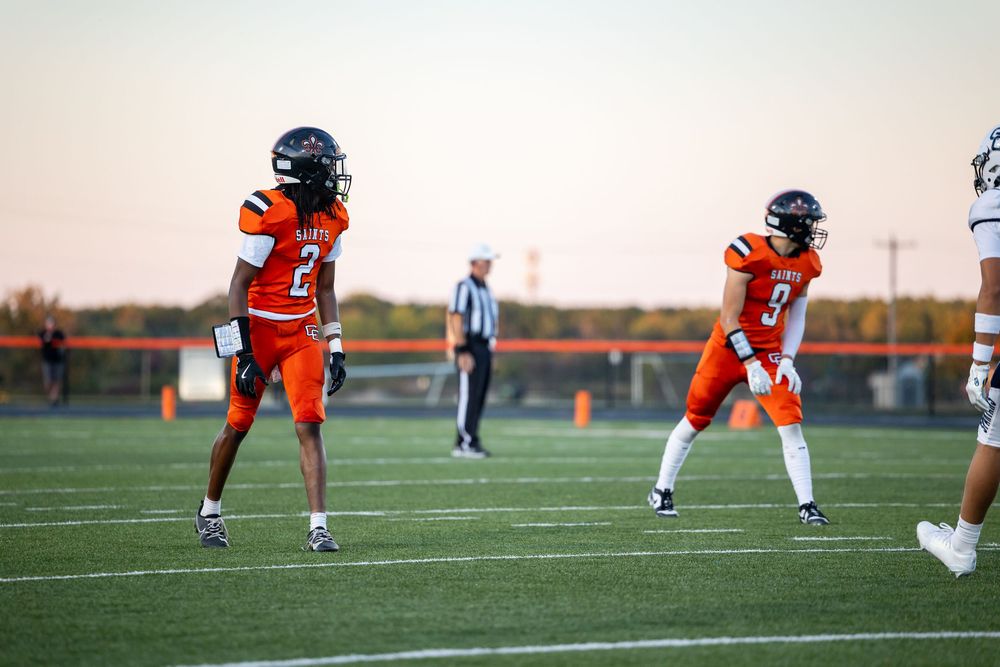 Football players in orange and white uniforms line up on field during game.