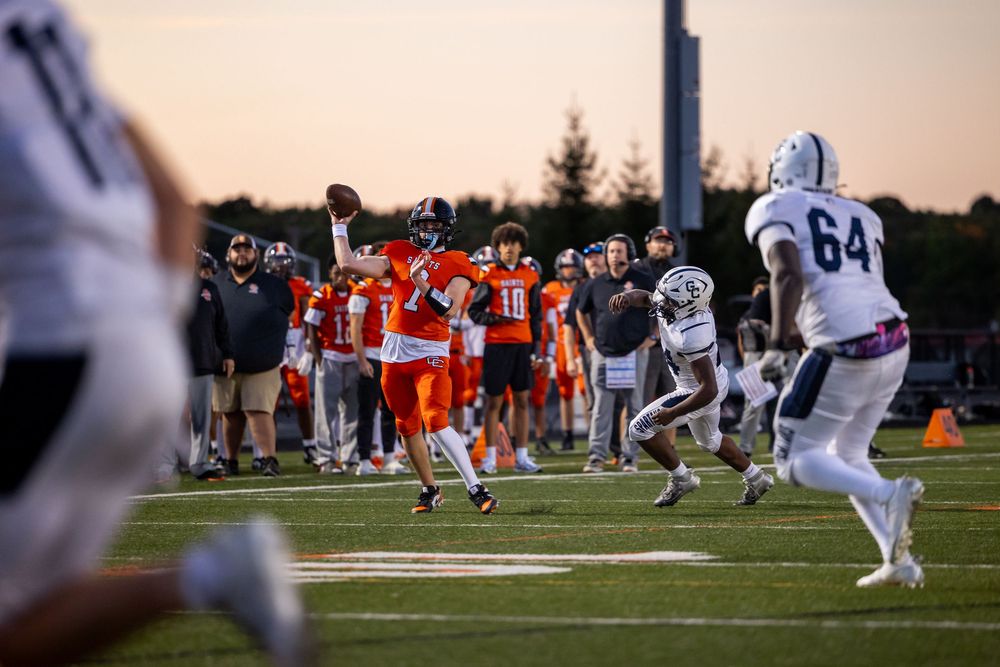 Football players from opposing teams face off at line of scrimmage during sunset game.
