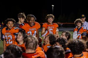 Football team in orange jerseys celebrates on sideline during night game.