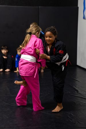 Two martial arts students practicing techniques in a training studio with black mats.