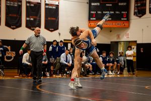 High school wrestlers compete on mats during an indoor wrestling match.