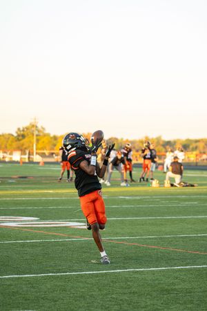 Player in orange uniform practices kicking drills on football field at sunset.