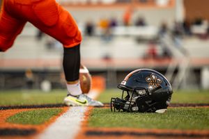 Black football helmet with team logo rests on field next to player's cleats.