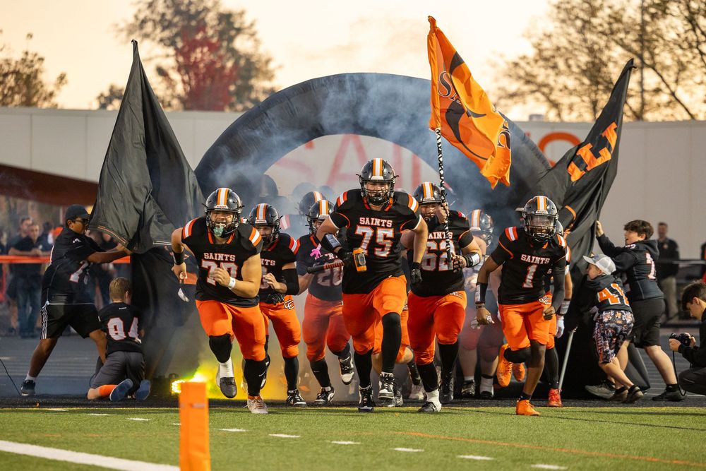 Football team runs onto field through smoke and flags during dramatic game entrance.