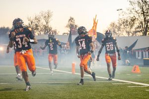 Players in orange jerseys celebrate on misty football field during evening game.